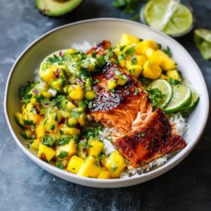 Mango salsa salmon bowl with crispy-skinned pan-seared salmon over white rice, bright orange mango salsa with red bell pepper, avocado slices, lime wedges, fresh cilantro